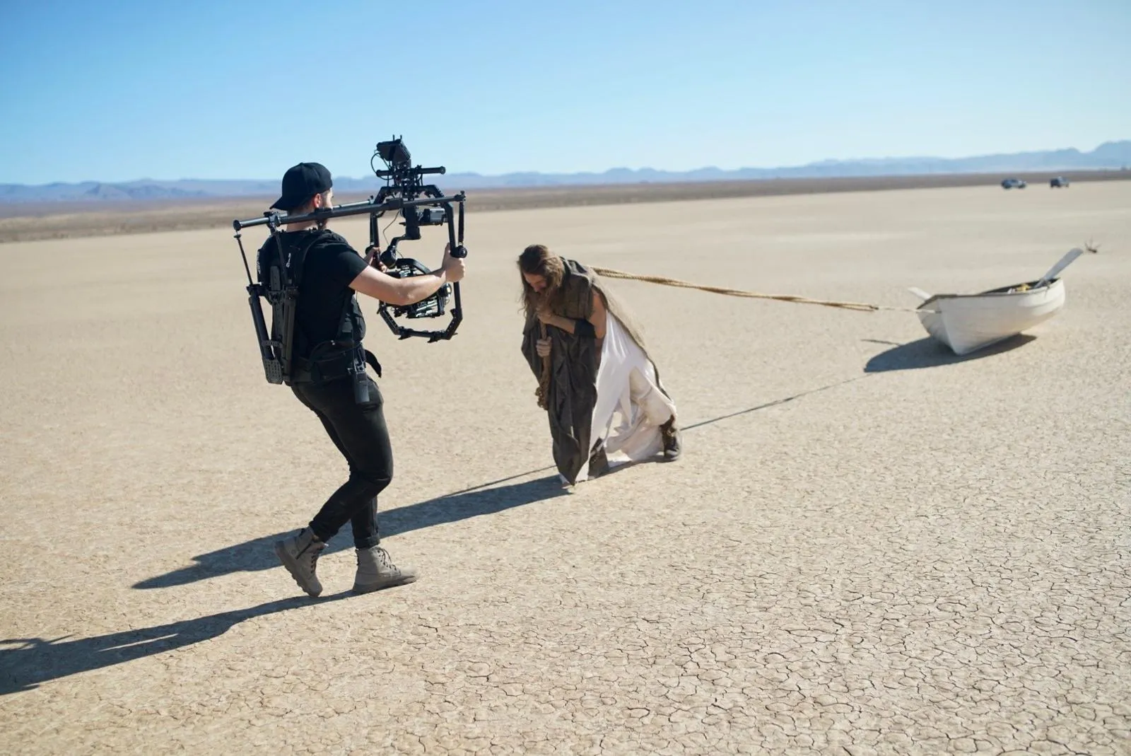A camera operator with a gimbal following a performer across a dry lakebed