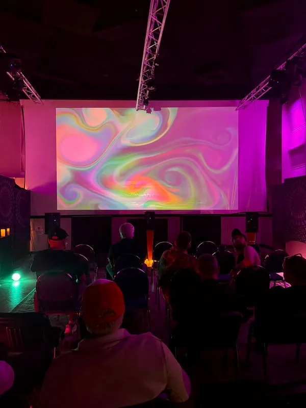 A darkened room of listeners facing a projected swirl of color