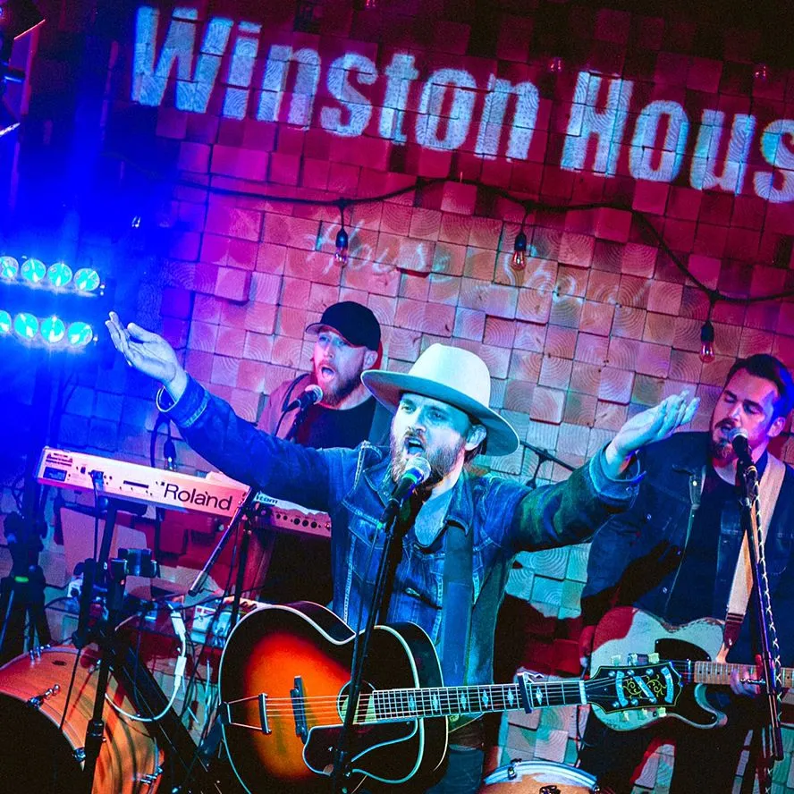 A band on stage under Winston House neon